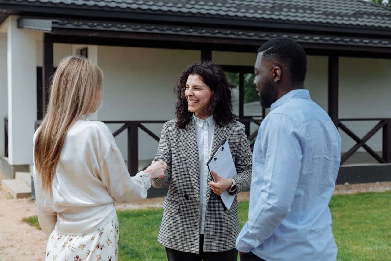 A professional real estate meeting taking place outside a house with three individuals engaging in conversation.