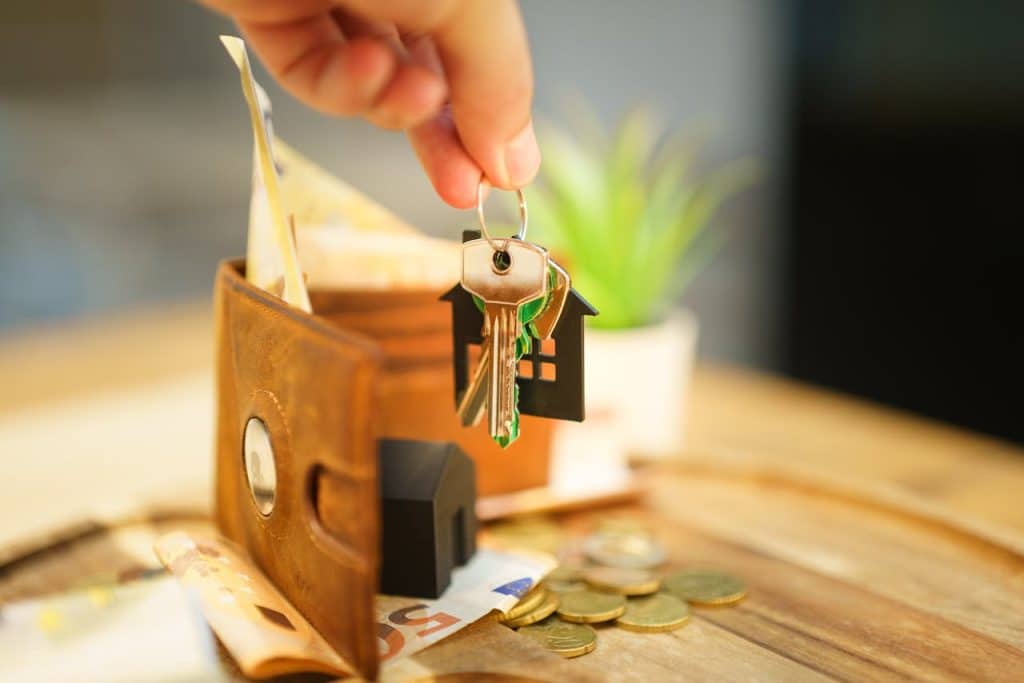 A hand holding a key above a small model of a house, symbolizing home ownership and new beginnings.