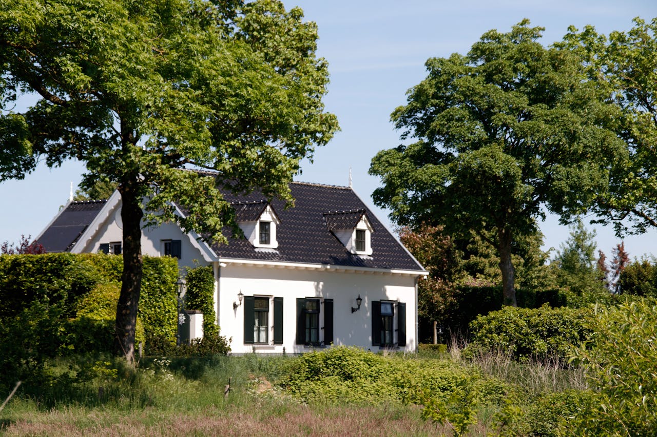 A charming white cottage with a black roof nestled among trees.