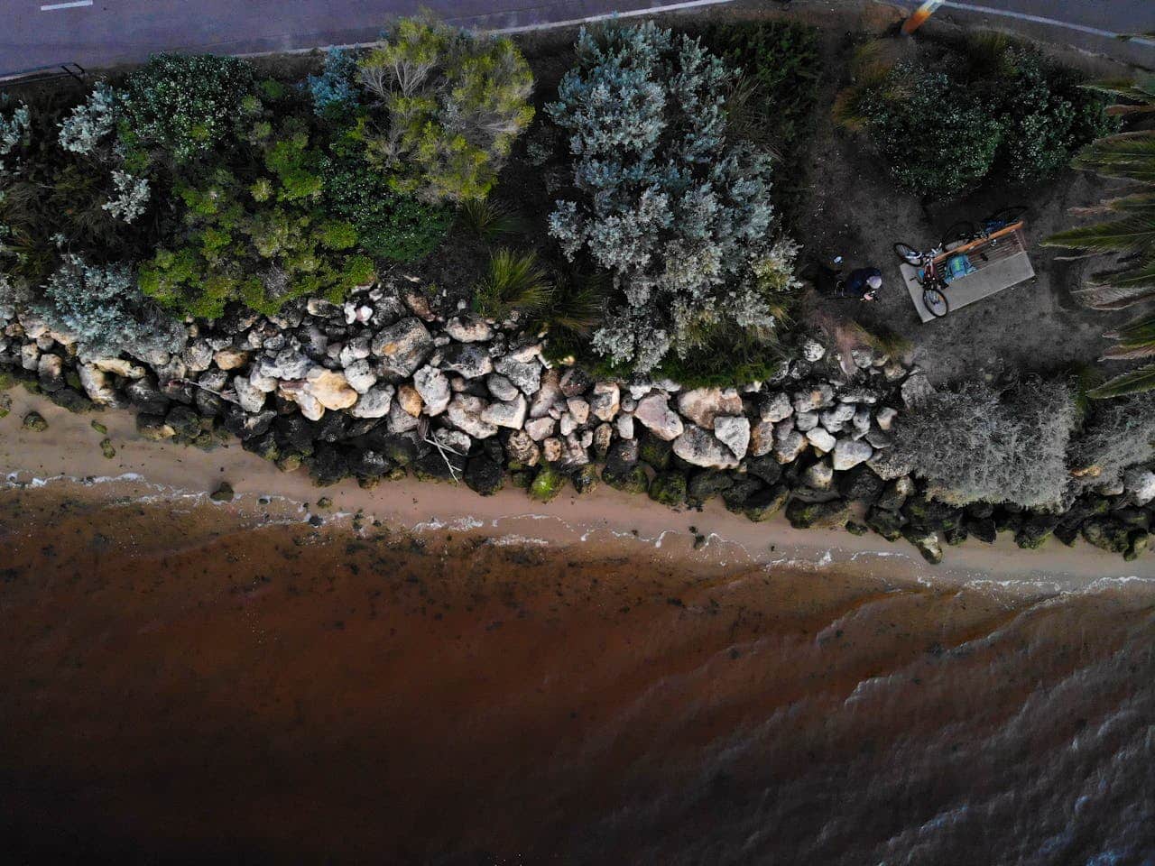 Aerial view of a rocky shoreline with vegetation and a bike near the water.