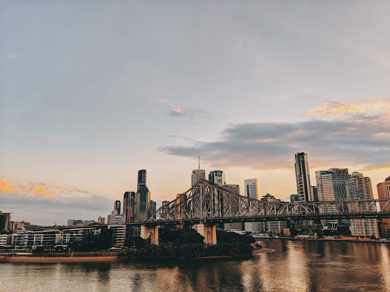 A stunning view of Brisbane city during sunset with the iconic bridge and skyline reflected in the river.