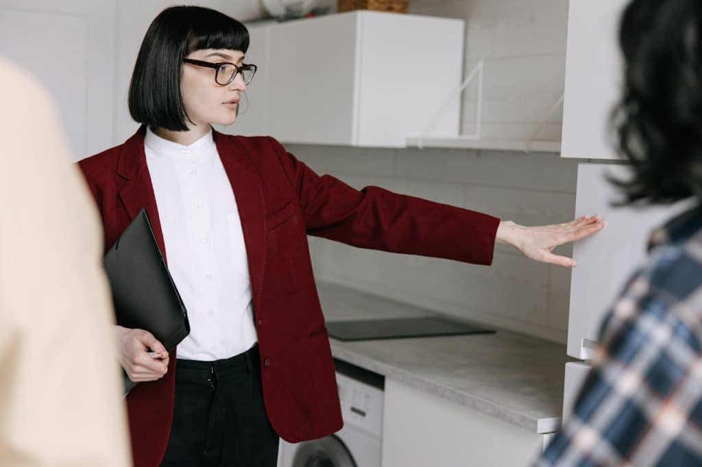 A professional woman in a burgundy blazer explaining kitchen design concepts while pointing at cabinets.