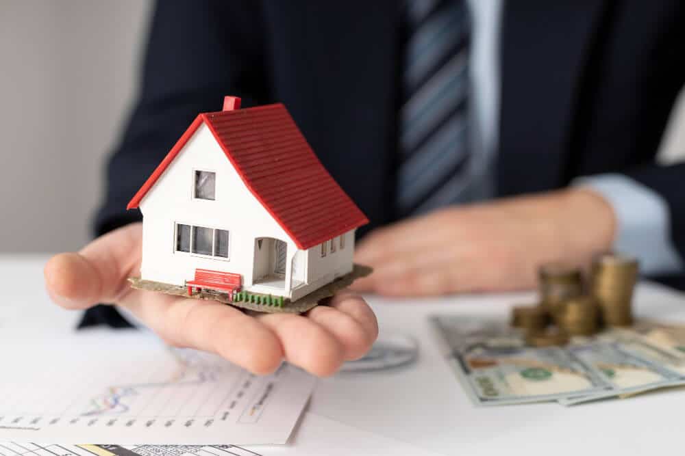 A person holding a miniature house representing real estate investment.