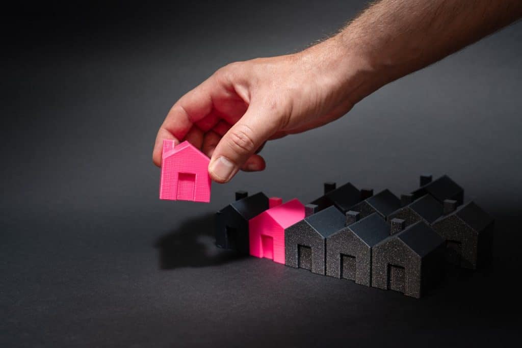 A hand placing a pink house among black houses, symbolizing choice and individuality in real estate.