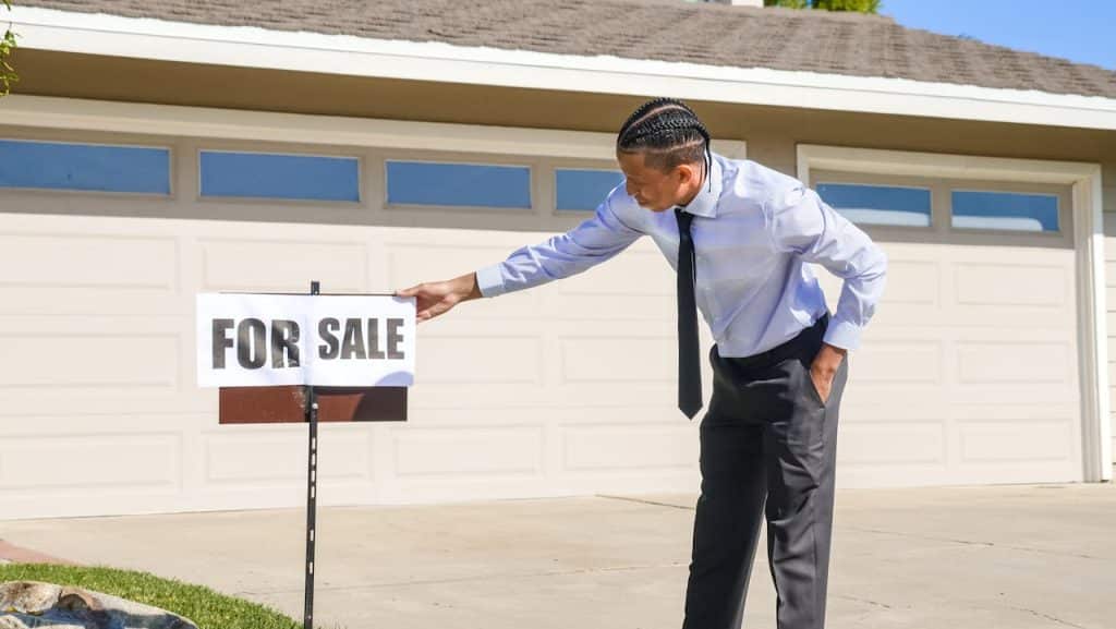 A man adjusting a 'For Sale' sign in front of a house.