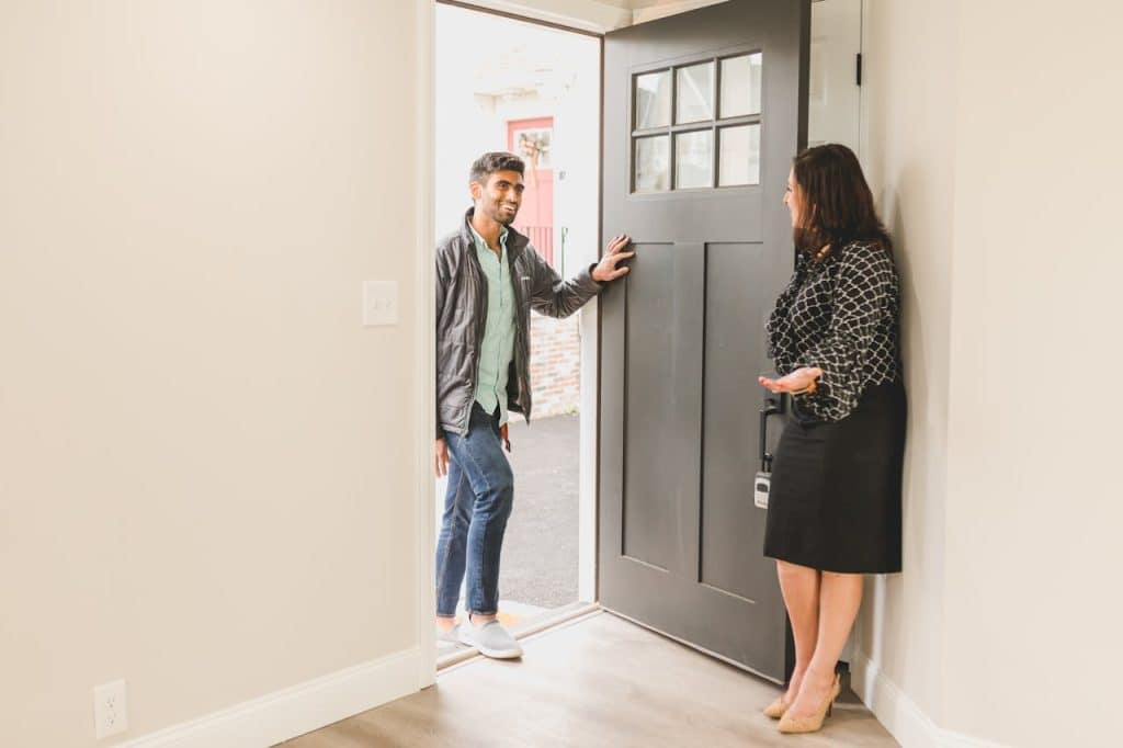 A man being welcomed at the door by a woman in a stylish outfit.