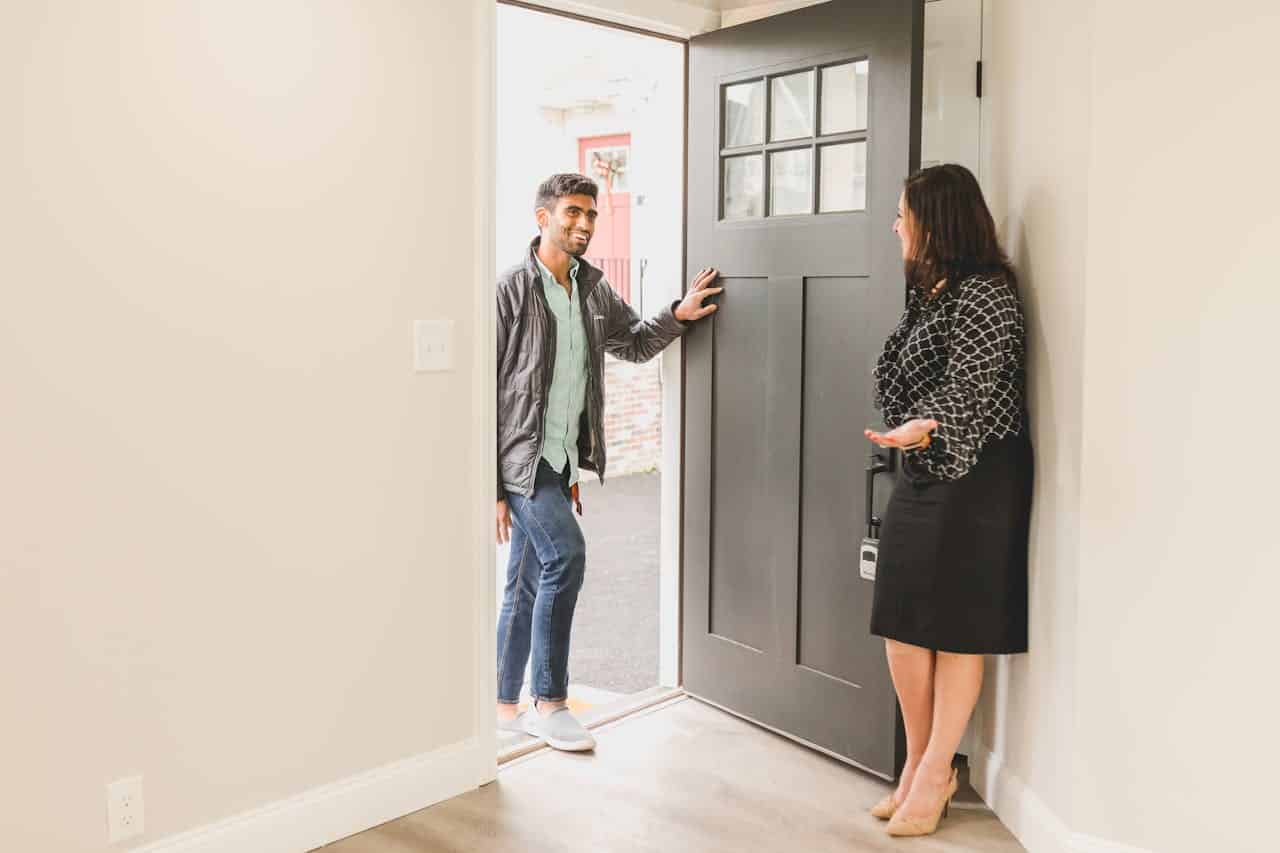 A man being welcomed at the door by a woman in a stylish outfit.