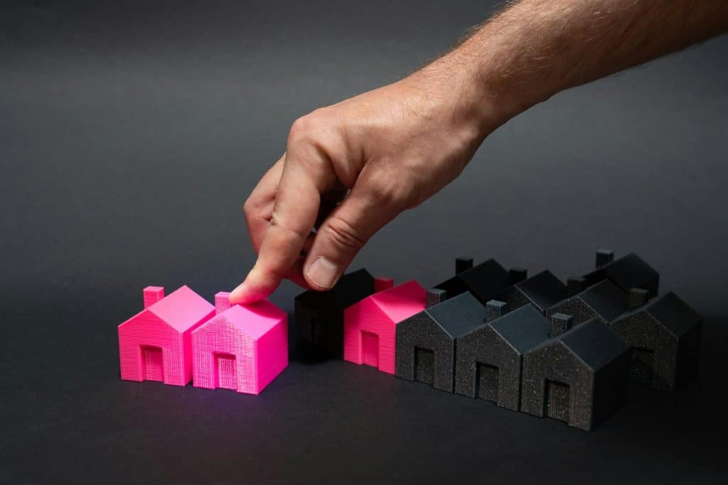 A hand selecting a pink house among black houses on a dark background.