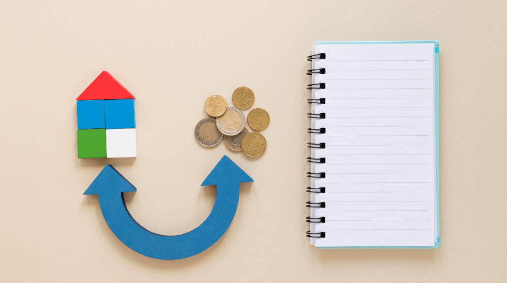 A colorful house model, coins, and a blank notebook on a beige background.