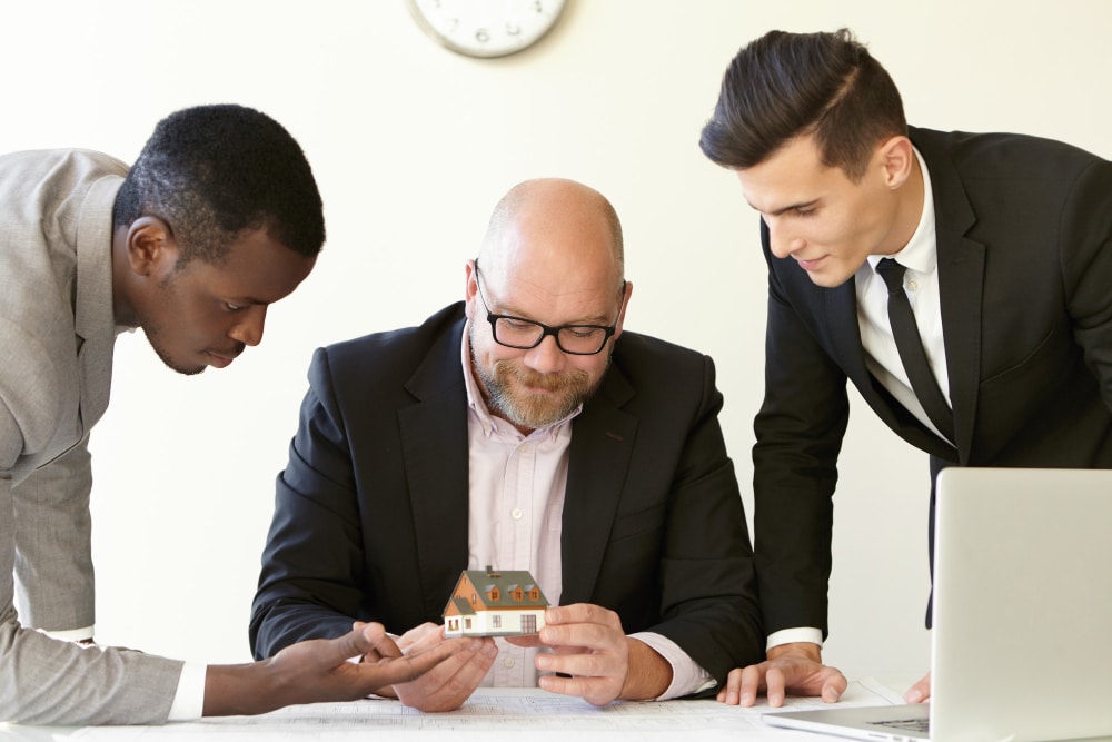Three professionals discussing a model house during a real estate consultation.