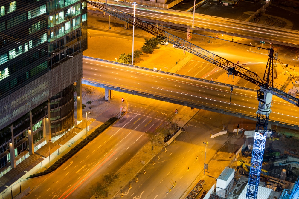 Aerial view of a cityscape at night with a construction crane and illuminated roads.