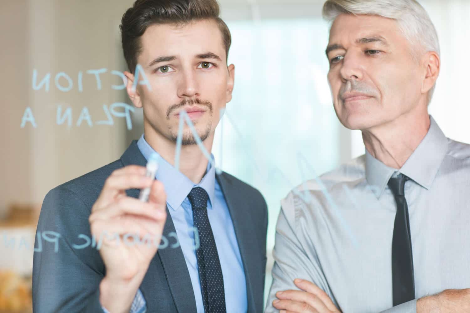 Two professionals discussing a strategic business plan on a glass board.
