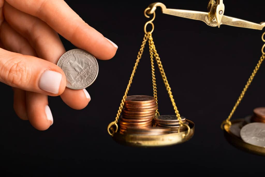 A hand holding a quarter above a scale with various coins.