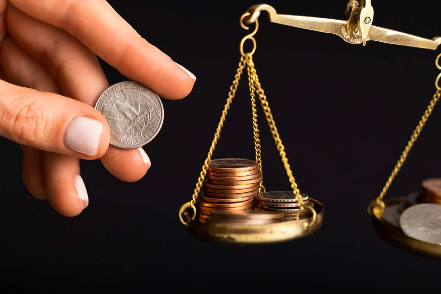 A hand holding a quarter above a scale with various coins.