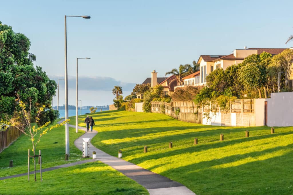 A scenic pathway along the waterfront with lush green grass and houses.
