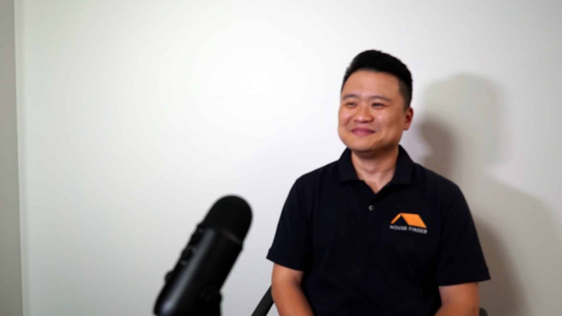 Simon Loo, founder of House Finder, in a branded House Finder polo seated beside a microphone