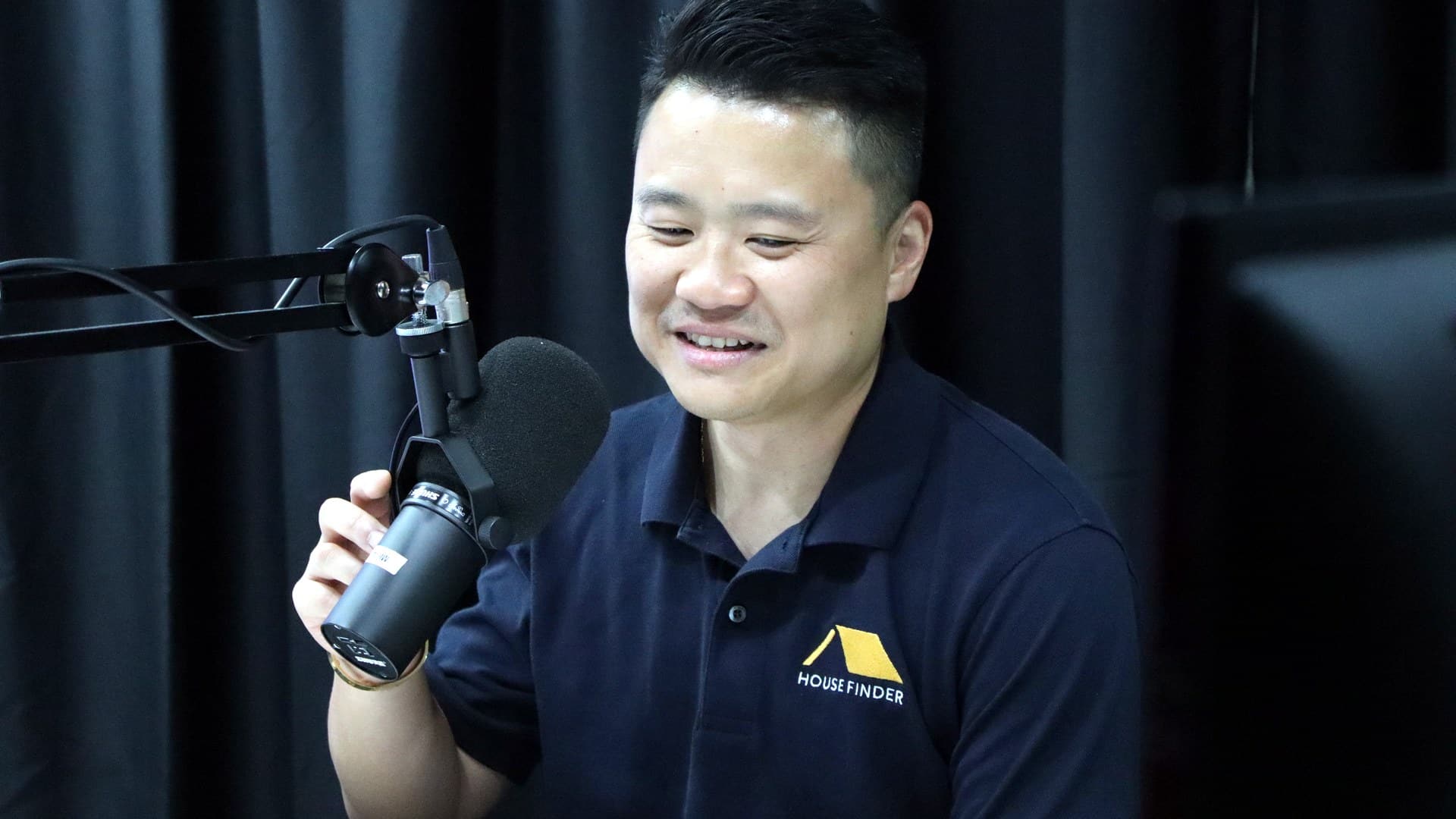 Simon Loo, founder of House Finder, speaking into a podcast microphone in a branded polo