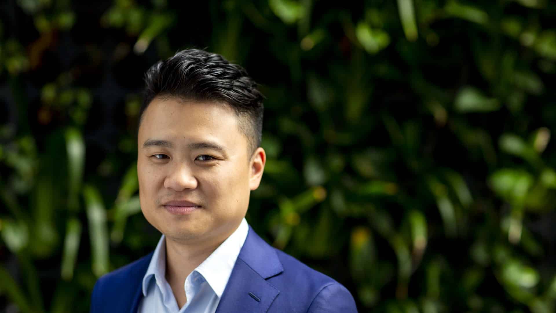 Close portrait of Simon Loo, founder of House Finder, in a navy blazer against dark foliage